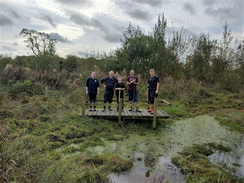 A group of five people standing on a wooden platform over a pond.