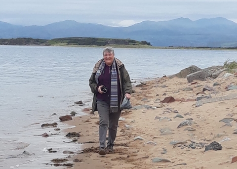 A woman walking along the shoreline with mountains in the background