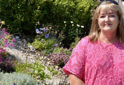 A woman dressed in pink standing beside a bed of flowers and shrubs