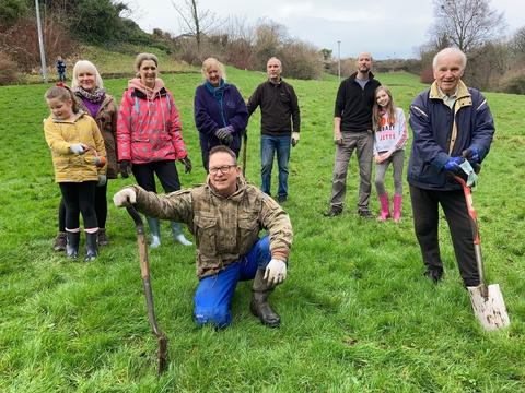 A group of people of various ages standing in a field, holding gardening tools