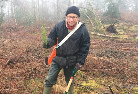 A man holding a small plant and a spade 