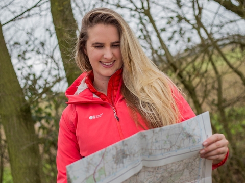 A young woman with long hair and a red coat reading a map