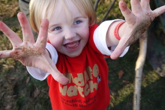 child with muddy hands wearing a Wildlife Trust Wildife Watch tee shirt