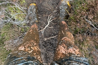 A view from someone looking down at their feet and legs, which are covered in mud from running in the Lakeland fells. 