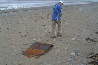 Volunteer dragging a large piece of metal from the beach