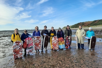 Image of nine people on beach with body boards about to collect seagrass seed