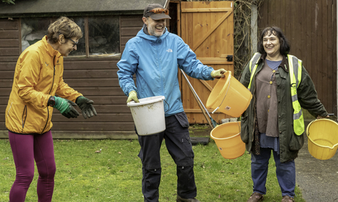 Three people outdoors in a garden holding buckets © Penny Dixie