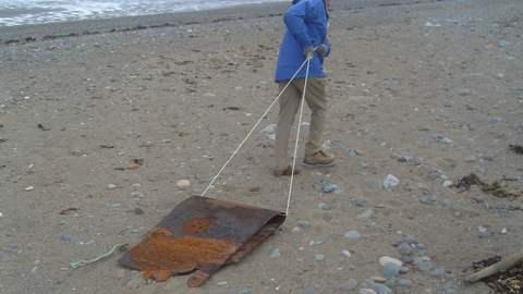 Volunteer dragging a large piece of metal from the beach